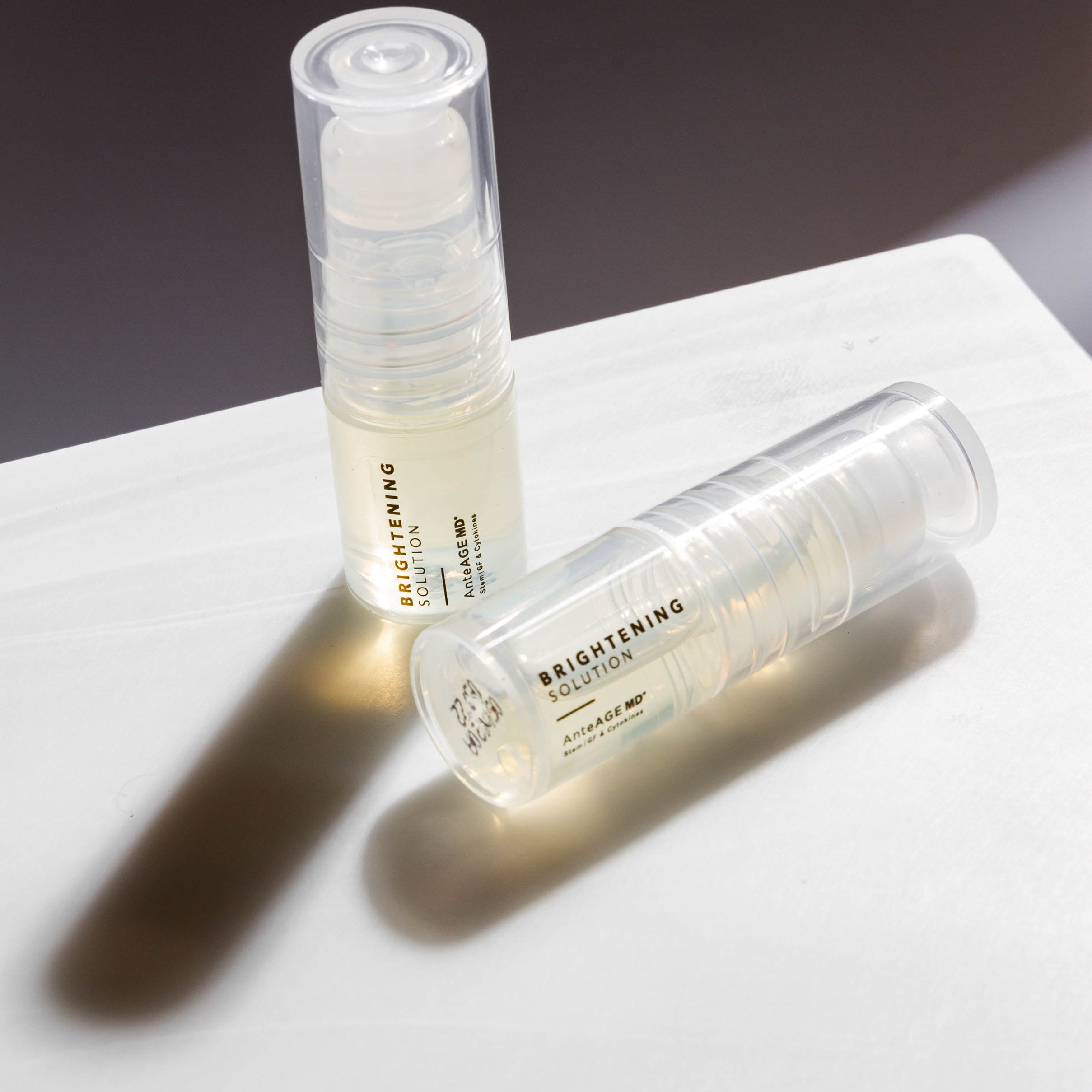 Two skincare serum bottles labeled 'Brightening' on a marble surface with a dark background.