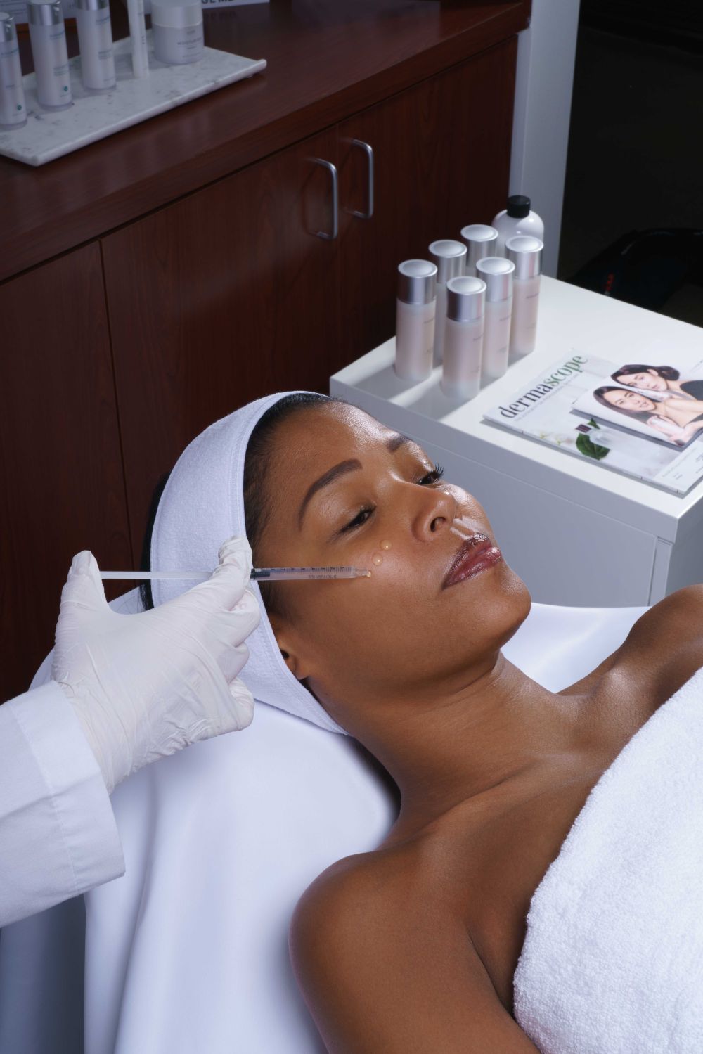 Woman receiving facial treatment in a spa setting with AnteAGE skincare products on a counter.